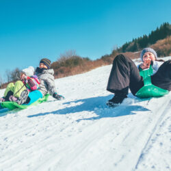 Happy laughing kids sliding down from the snow slope riding sleighs. Funny winter holidays spending concept image.