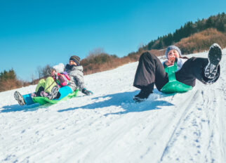 Happy laughing kids sliding down from the snow slope riding sleighs. Funny winter holidays spending concept image.