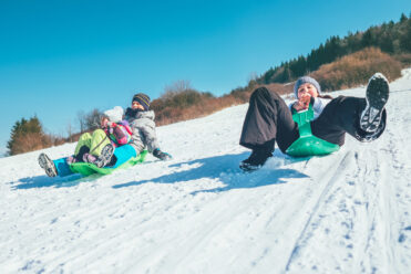 Happy laughing kids sliding down from the snow slope riding sleighs. Funny winter holidays spending concept image.