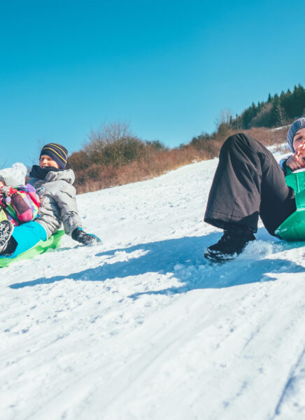 Happy laughing kids sliding down from the snow slope riding sleighs. Funny winter holidays spending concept image.